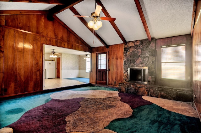 carpeted living room with wooden walls, a fireplace, ceiling fan, and a textured ceiling