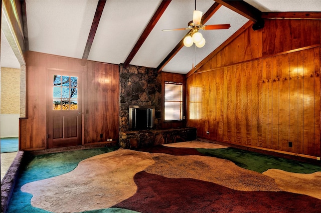 carpeted living room featuring a stone fireplace, ceiling fan, lofted ceiling with beams, and wood walls