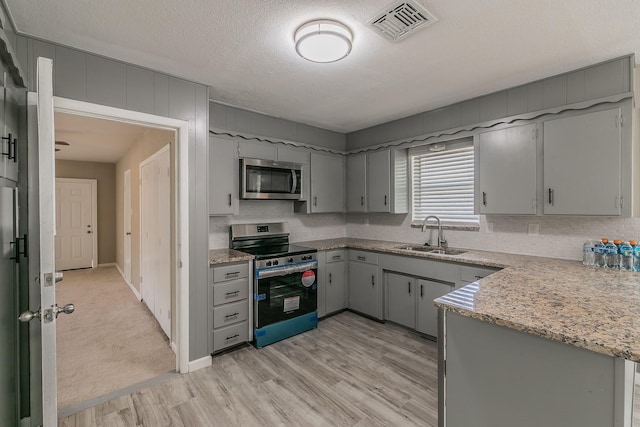 kitchen featuring sink, a textured ceiling, light wood-type flooring, appliances with stainless steel finishes, and kitchen peninsula