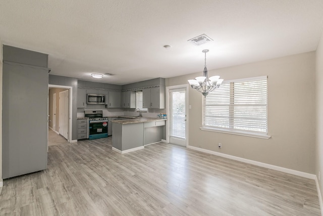 kitchen with gray cabinetry, appliances with stainless steel finishes, kitchen peninsula, pendant lighting, and light hardwood / wood-style floors