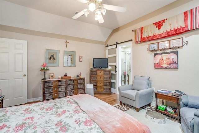 bedroom featuring ensuite bathroom, vaulted ceiling, ceiling fan, a barn door, and light hardwood / wood-style floors