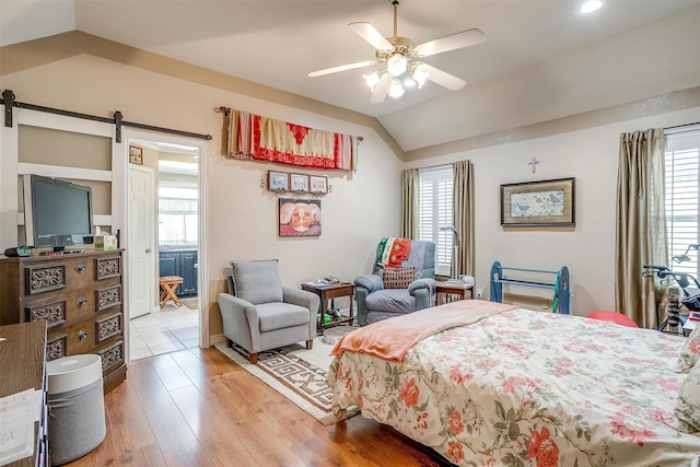 bedroom featuring ceiling fan, a barn door, wood-type flooring, and vaulted ceiling