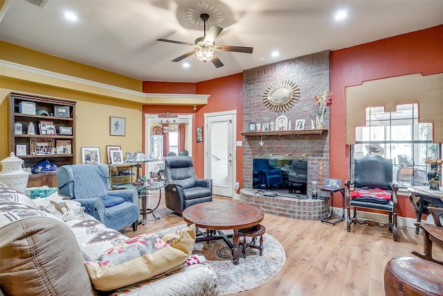 living room with a brick fireplace, ceiling fan, and light hardwood / wood-style flooring