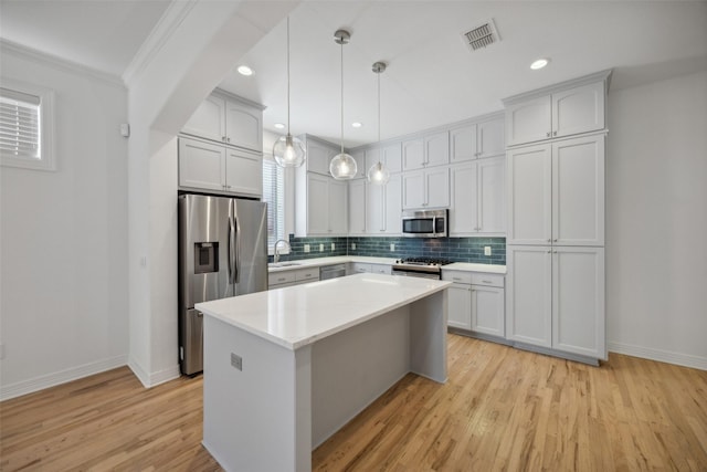 kitchen featuring sink, stainless steel appliances, a kitchen island, decorative light fixtures, and white cabinets