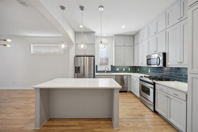 kitchen with sink, a center island, light hardwood / wood-style floors, decorative light fixtures, and appliances with stainless steel finishes