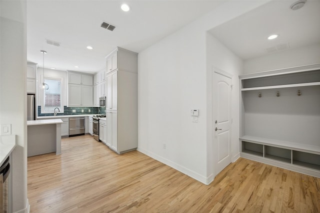 kitchen with decorative light fixtures, backsplash, stainless steel appliances, and light hardwood / wood-style flooring