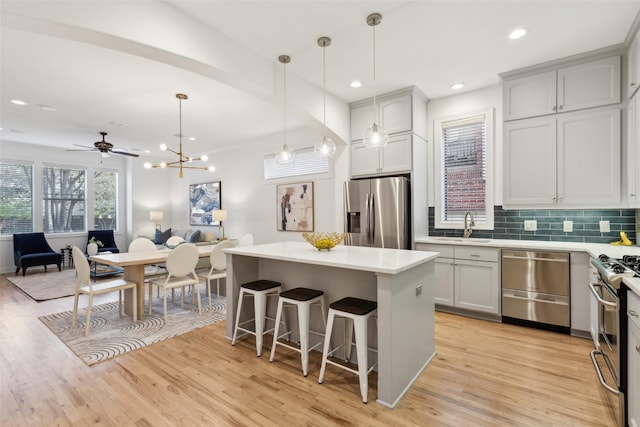 kitchen with appliances with stainless steel finishes, backsplash, ceiling fan with notable chandelier, a kitchen island, and hanging light fixtures