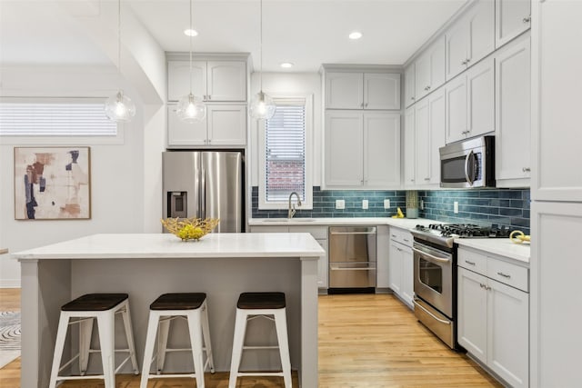 kitchen with appliances with stainless steel finishes, decorative light fixtures, a kitchen island, and sink