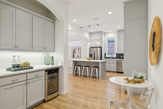 kitchen featuring wine cooler, light hardwood / wood-style flooring, appliances with stainless steel finishes, decorative light fixtures, and a breakfast bar area