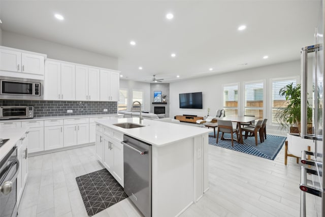 kitchen with white cabinets, appliances with stainless steel finishes, a kitchen island with sink, and sink