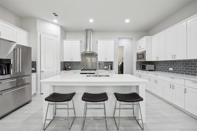 kitchen featuring white cabinets, stainless steel appliances, a center island with sink, and wall chimney exhaust hood