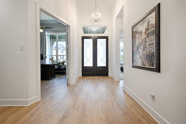 entrance foyer with french doors, light wood-type flooring, and ceiling fan with notable chandelier