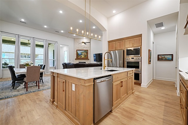 kitchen featuring appliances with stainless steel finishes, light hardwood / wood-style floors, sink, and a center island with sink