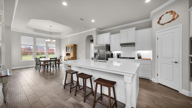 kitchen featuring a breakfast bar, a large island with sink, white cabinets, stainless steel fridge, and a notable chandelier