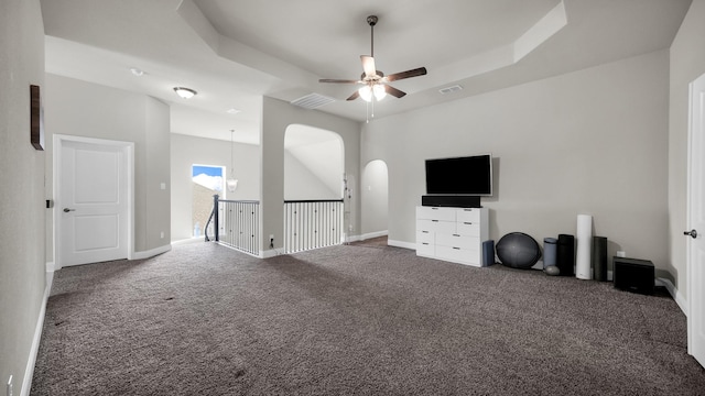 unfurnished living room with a tray ceiling, ceiling fan, and dark carpet