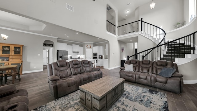 living room featuring a towering ceiling, dark hardwood / wood-style flooring, crown molding, sink, and an inviting chandelier