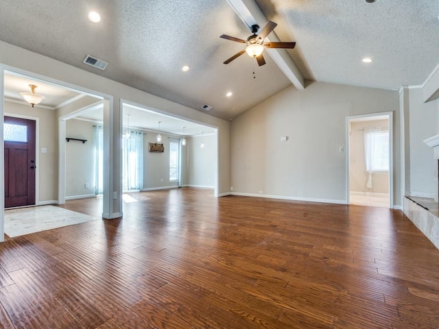 unfurnished living room featuring a textured ceiling, ceiling fan, a tile fireplace, hardwood / wood-style floors, and vaulted ceiling with beams