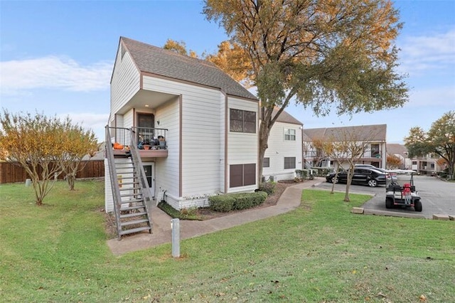 exterior space featuring a shingled roof, fence, a lawn, and stairs