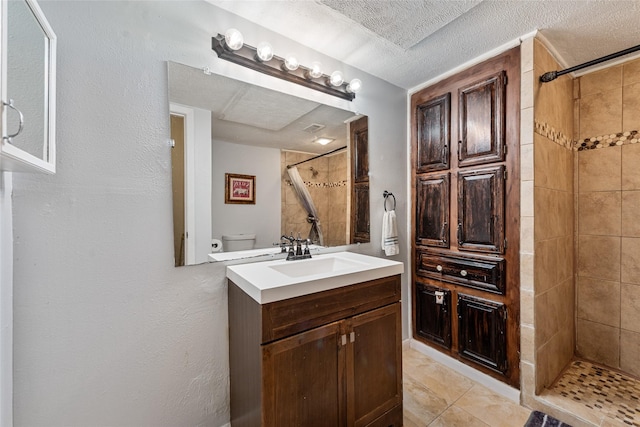 bathroom with tiled shower, toilet, a textured ceiling, and vanity