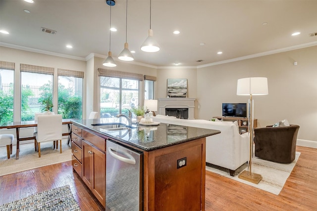 kitchen featuring a center island with sink, sink, light hardwood / wood-style flooring, dark stone countertops, and decorative light fixtures