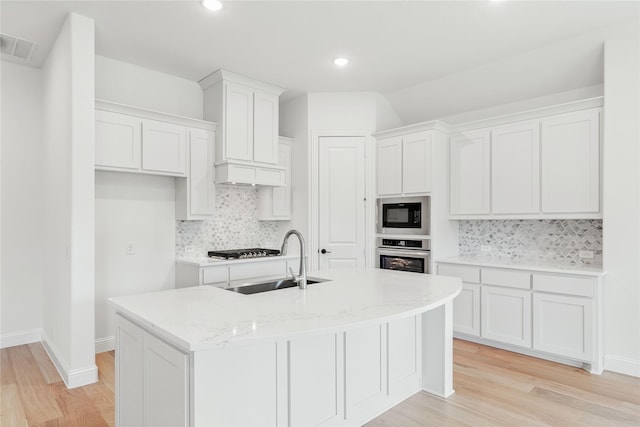 kitchen featuring dark wood-type flooring, sink, appliances with stainless steel finishes, a kitchen island with sink, and decorative backsplash