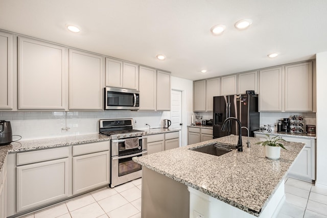 kitchen featuring sink, stainless steel appliances, light stone counters, a kitchen island with sink, and light tile patterned flooring