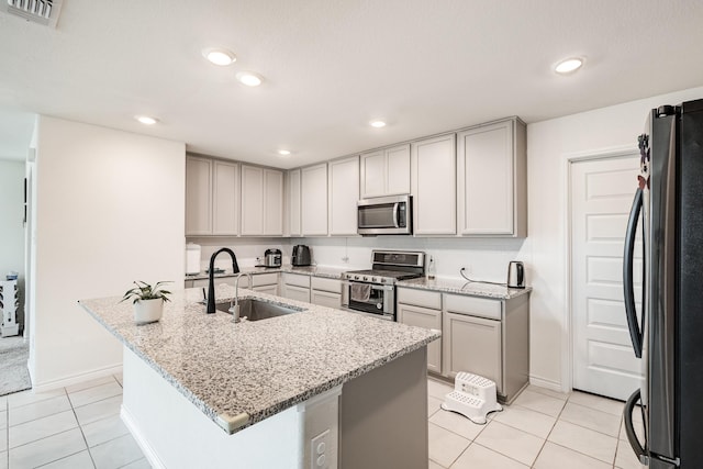 kitchen featuring light stone countertops, stainless steel appliances, a kitchen island with sink, sink, and light tile patterned flooring