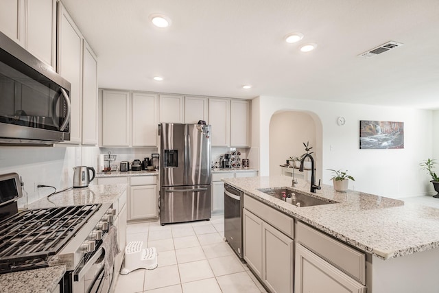 kitchen with a kitchen island with sink, sink, light stone countertops, appliances with stainless steel finishes, and light tile patterned flooring