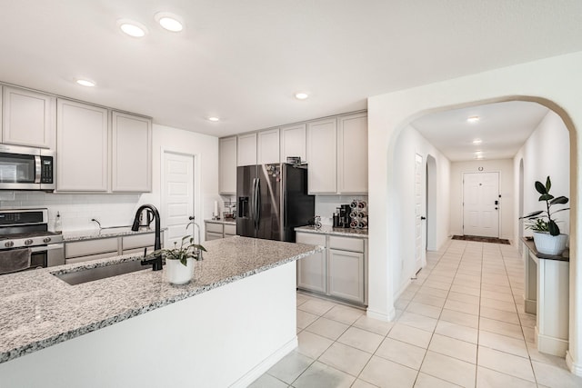 kitchen featuring backsplash, sink, appliances with stainless steel finishes, light tile patterned flooring, and light stone counters