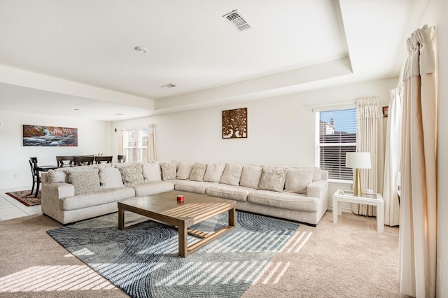 living room with a tray ceiling and light carpet