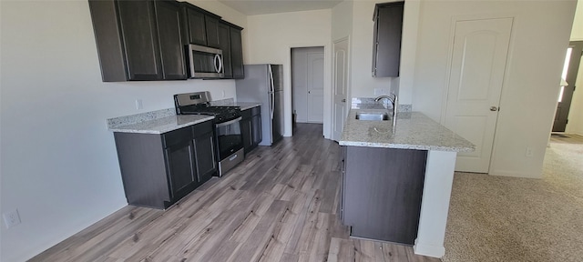 kitchen with light stone countertops, appliances with stainless steel finishes, light hardwood / wood-style floors, and sink