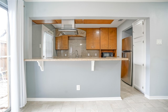 kitchen featuring a kitchen bar, stainless steel refrigerator, kitchen peninsula, and tasteful backsplash