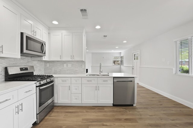 kitchen with appliances with stainless steel finishes, kitchen peninsula, dark hardwood / wood-style floors, sink, and white cabinetry