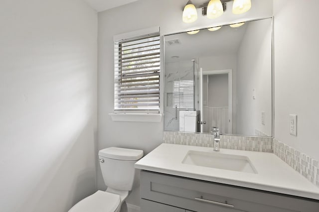 bathroom featuring toilet, vanity, a shower with shower door, and tasteful backsplash