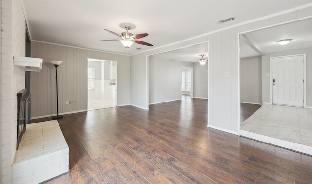 unfurnished living room with crown molding, dark hardwood / wood-style flooring, ceiling fan, and a fireplace