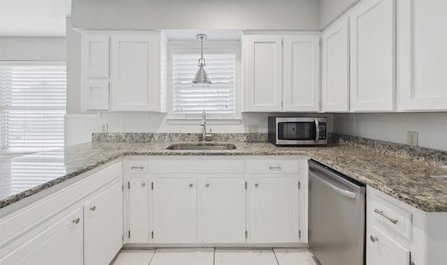 kitchen with appliances with stainless steel finishes, stone countertops, white cabinetry, sink, and hanging light fixtures