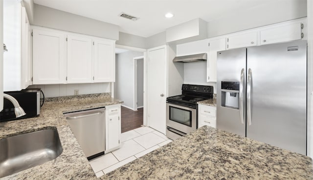 kitchen featuring wall chimney range hood, stainless steel appliances, light stone countertops, white cabinets, and light tile patterned flooring