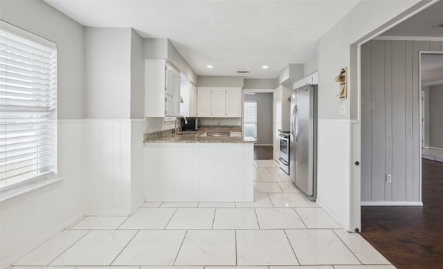 kitchen with sink, white cabinetry, stone countertops, stainless steel fridge, and kitchen peninsula