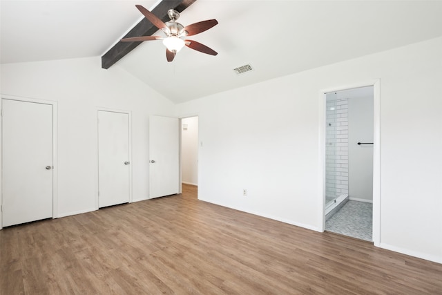 unfurnished bedroom featuring vaulted ceiling with beams, two closets, connected bathroom, and light wood-type flooring