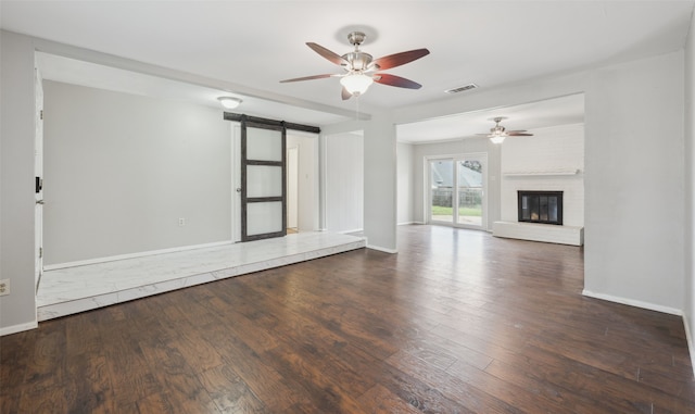 unfurnished living room featuring dark hardwood / wood-style floors, a fireplace, a barn door, and ceiling fan