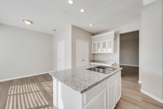 kitchen with a center island, white cabinets, light hardwood / wood-style flooring, black electric cooktop, and light stone counters