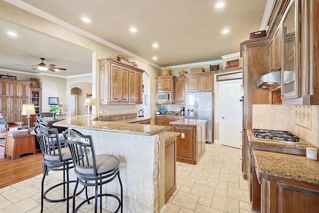 kitchen with a kitchen breakfast bar, ceiling fan, light stone counters, kitchen peninsula, and stainless steel appliances