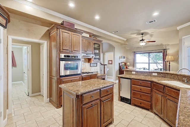 kitchen with light stone countertops, sink, stainless steel appliances, crown molding, and a kitchen island