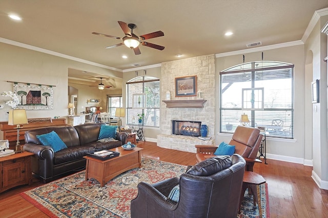 living room featuring hardwood / wood-style flooring, ceiling fan, a stone fireplace, and ornamental molding