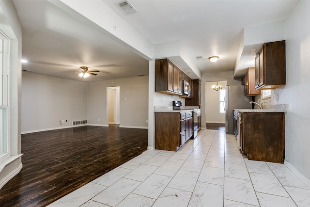 kitchen with light wood-type flooring, appliances with stainless steel finishes, ceiling fan with notable chandelier, and dark brown cabinets