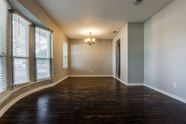 empty room with dark wood-type flooring and an inviting chandelier