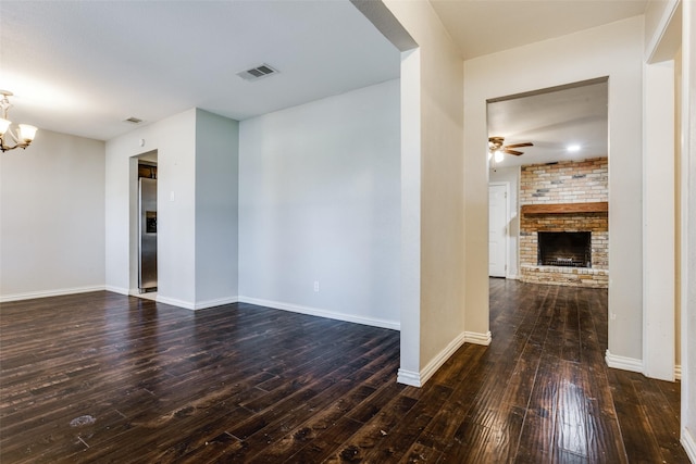 empty room with dark wood-type flooring, a fireplace, and ceiling fan with notable chandelier