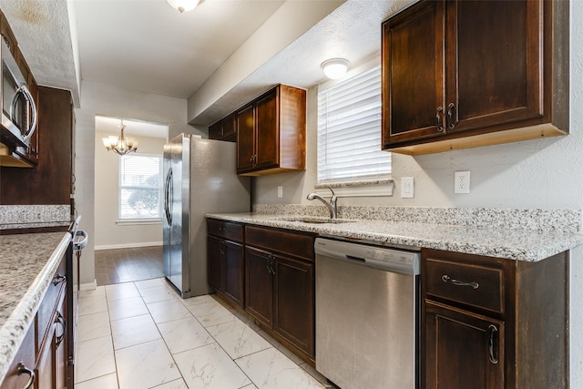 kitchen with light stone countertops, stainless steel appliances, a chandelier, and sink