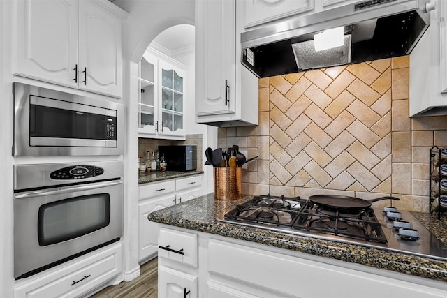 kitchen with ventilation hood, dark stone countertops, decorative backsplash, white cabinets, and appliances with stainless steel finishes