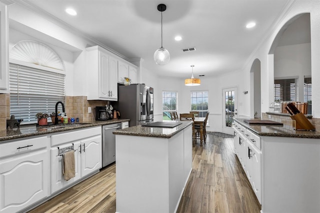 kitchen featuring appliances with stainless steel finishes, a sink, arched walkways, a center island, and visible vents
